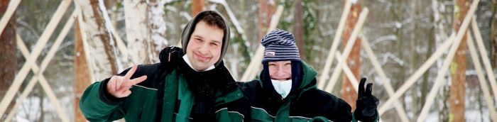 Zwei Mitarbeiter der Forstgruppe in grüner Winterkleidung zeigen Victory-Zeichen in die Kamera und lachen fröhlich