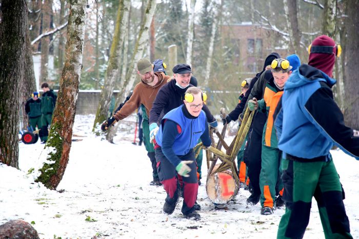 Mehrere Mitarbeiter unserer Forstgruppe ziehen fröhlich einen Baumstamm durch den Schnee, Winterarbeiten im Wald