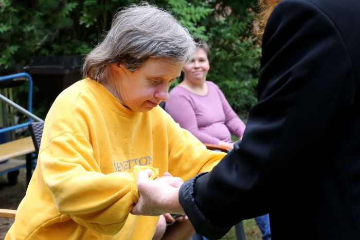 Eine Bewohnerin der LebensOrte im gelben Sweatshirt wird kraftvoll an den Händen geführt und zuversichtlich festgehalten