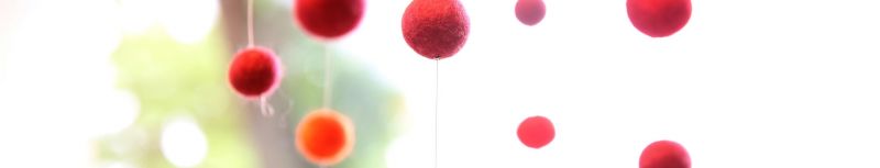 Rote kleine Filzbälle zu einer Kette genäht hängen von der Decke herunter