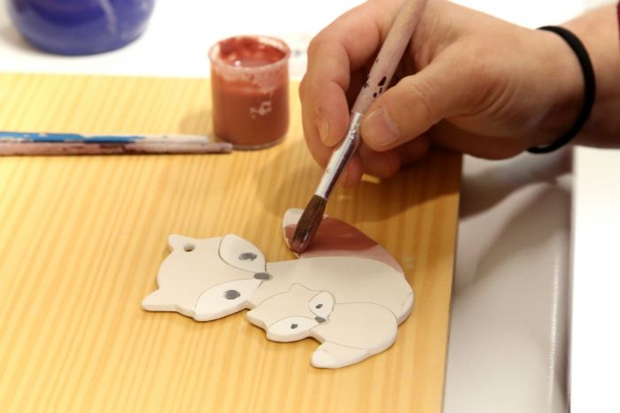 Hände einer Keramikerin, die mit Pinsel einen Fuchsanhänger bemalt