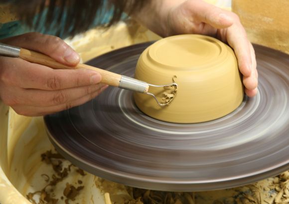 Hände einer Keramikerin an der Drehscheibe in Bewegung, eine Schale wird in unserer Keramikwerkstatt fertig erstellt